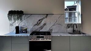 A modern kitchen with a marble backsplash, a built-in oven, a sink, and a window above the sink.