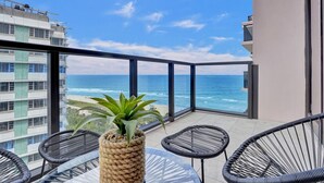Un balcon avec vue sur l’océan, des fauteuils en osier et une plante en pot.