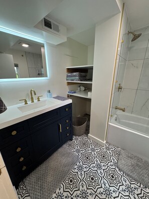 Een moderne badkamer met een wastafel met dubbele wastafel, een grote spiegel, een douche met glazen deur en vloertegels met een patroon.