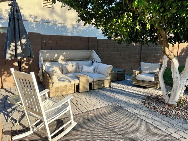 A patio with a wicker sofa, a white rocking chair, and a small table.