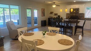 A spacious kitchen with white cabinets, a dining area with a round table and chairs, and a sliding glass door leading to a backyard. - Private retreat with gym, hot tub, pool & playroom (Phoenix)