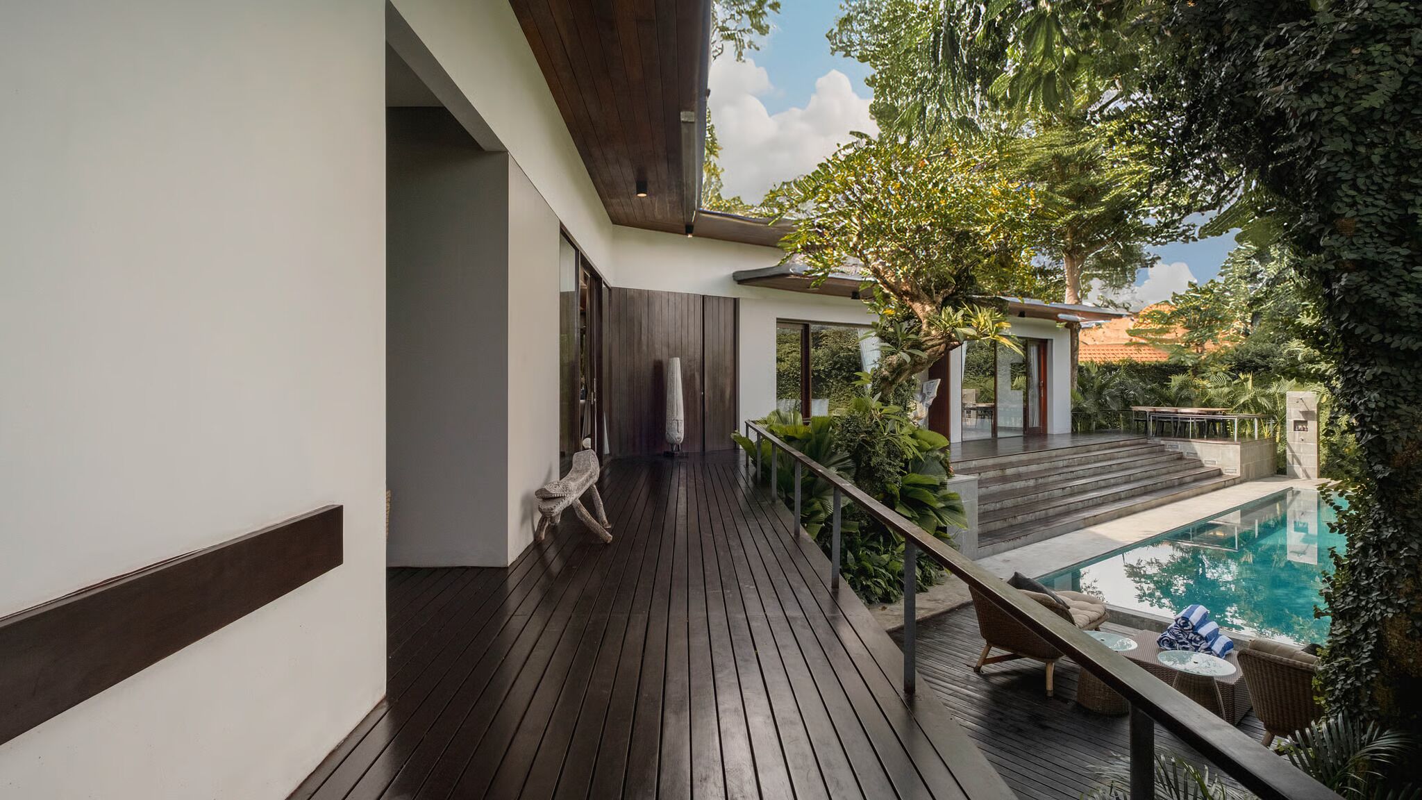A wooden deck with a pool, surrounded by greenery and a clear sky.