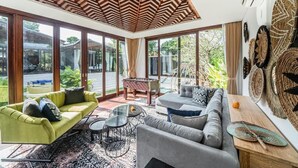 A modern living room with a large glass door leading to a garden, a wooden ceiling, and a dining area with a table and chairs. - De Prestigio Villa II (Canggu)