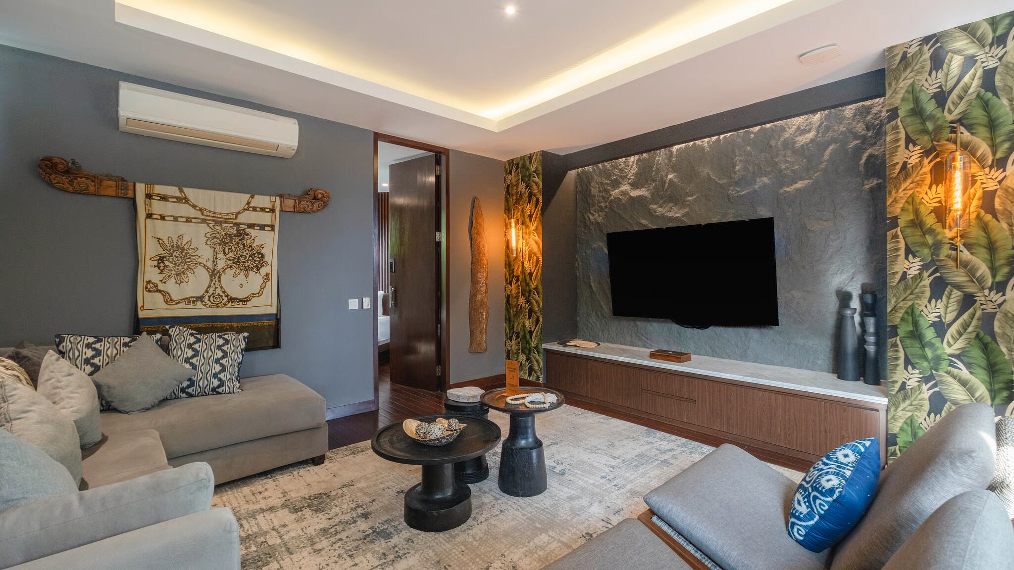 A modern living room with a sofa, coffee table, and a flat-screen TV mounted on a textured wall.