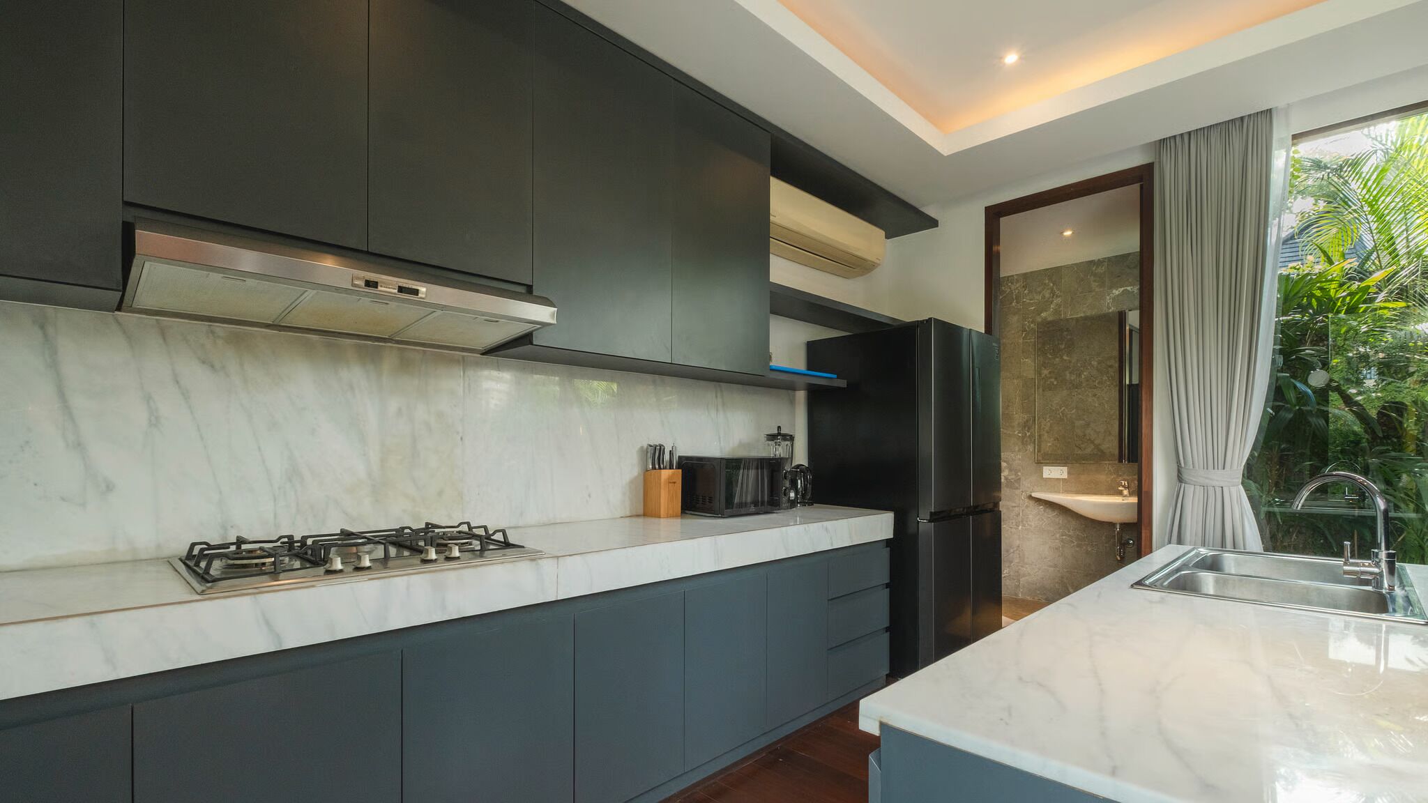 A modern kitchen with dark cabinets, a gas stove, a black refrigerator, and a marble countertop.