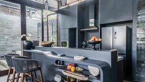 A modern kitchen with dark cabinetry, a curved island, and a bar area with stools. - De Prestigio Villa II (Canggu)