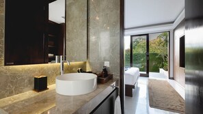 A modern bathroom with a large mirror, a round sink, and a view of a bedroom with a bed and a window. - De Prestigio Villa II (Canggu)