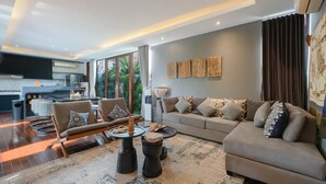 A modern living room with a sofa, chairs, a coffee table, and a kitchen area visible through a glass partition. - De Prestigio Villa II (Canggu)