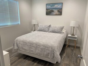 Une chambre à coucher avec un lit, deux tables de chevet avec des lampes, un tableau au mur et une fenêtre avec des stores.