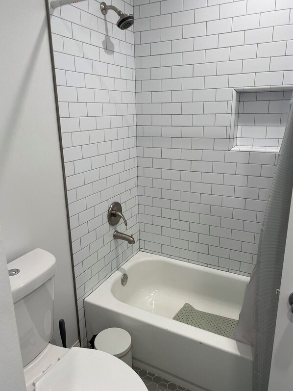 Un baño con azulejos blancos tipo metro, una bañera, un inodoro y un cabezal de ducha.