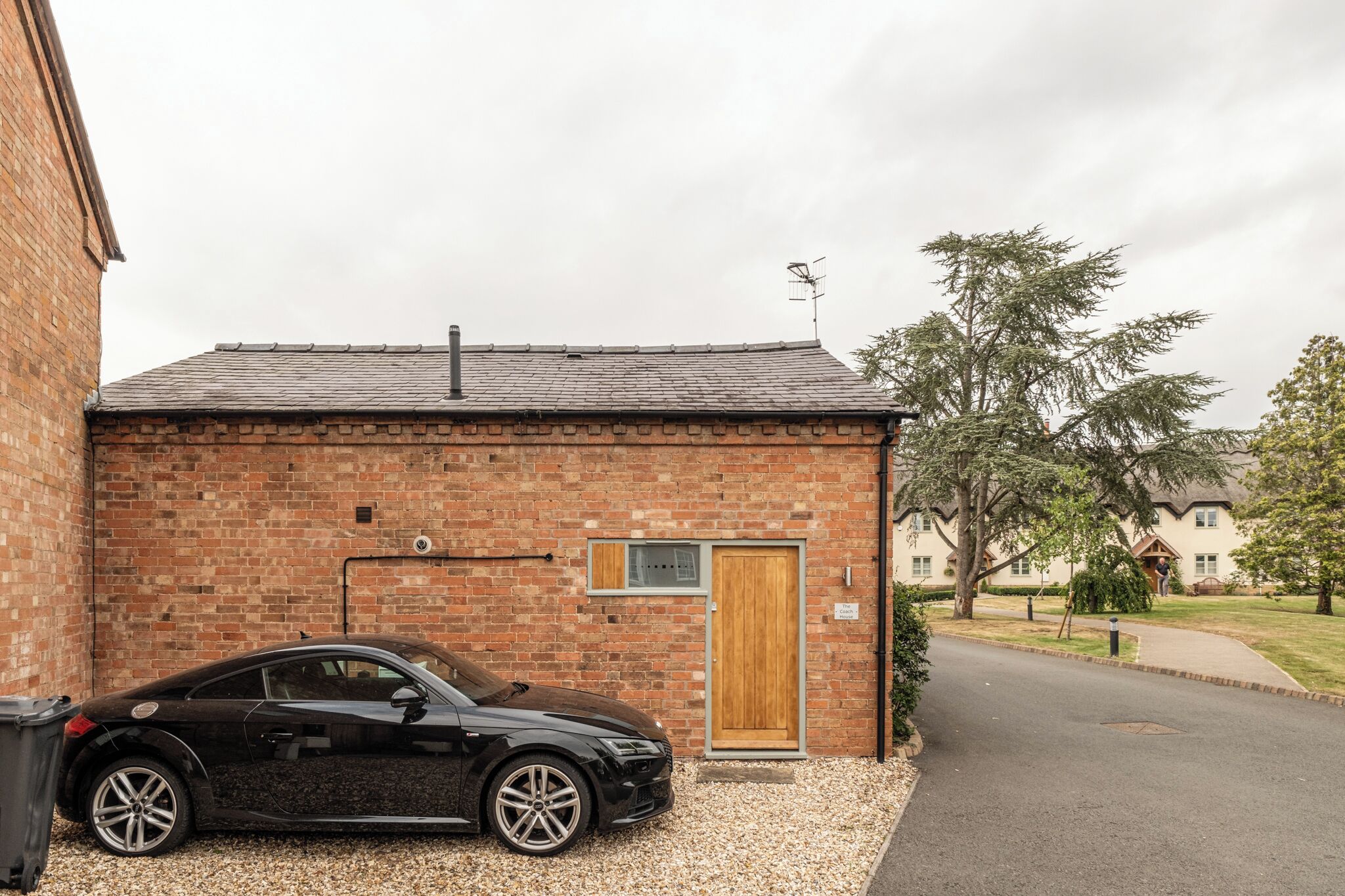 A black car parked in front of a brick building with a wooden door and a small window.