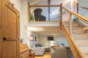A modern loft-style living area with a wooden staircase, a sofa set, a flat-screen TV, and a fireplace. - The Coach House Retreat in Warwickshire (Stratford-upon-Avon)