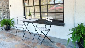A patio area with a table and chairs, a window with blinds, and potted plants.