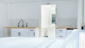 A modern hotel room with a large bed, a wooden bedside table, a white sink, and a mirror.