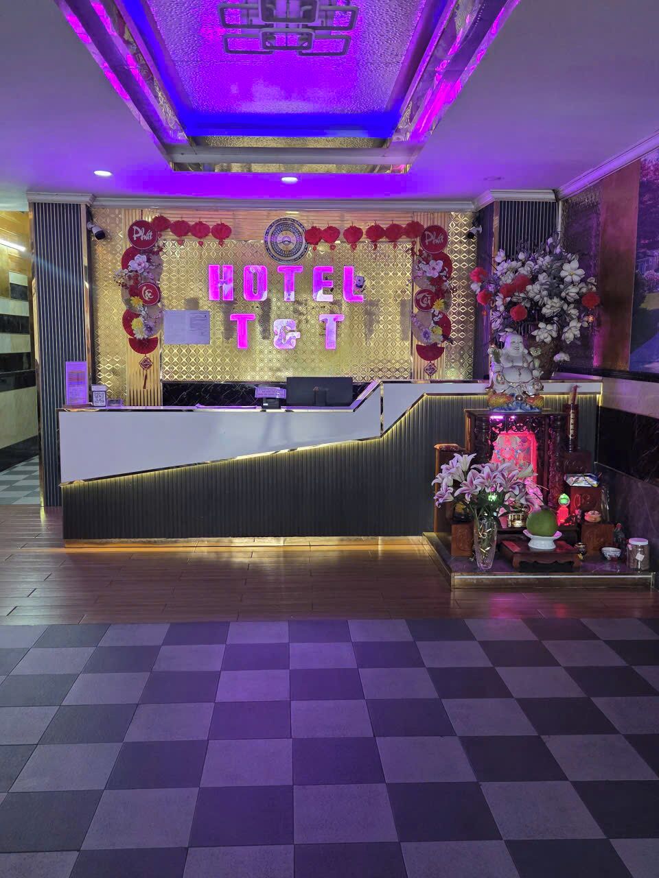 A hotel reception desk with a check-in counter, a decorative wall with floral arrangements, and a patterned floor.
