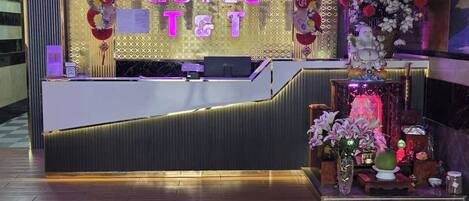 A hotel reception desk with a check-in counter, a decorative wall with floral arrangements, and a patterned floor.