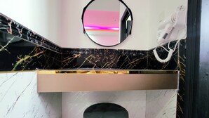 Une salle de bain avec un pare-baignoire en marbre noir et blanc, un miroir, un sèche-cheveux et un tabouret.