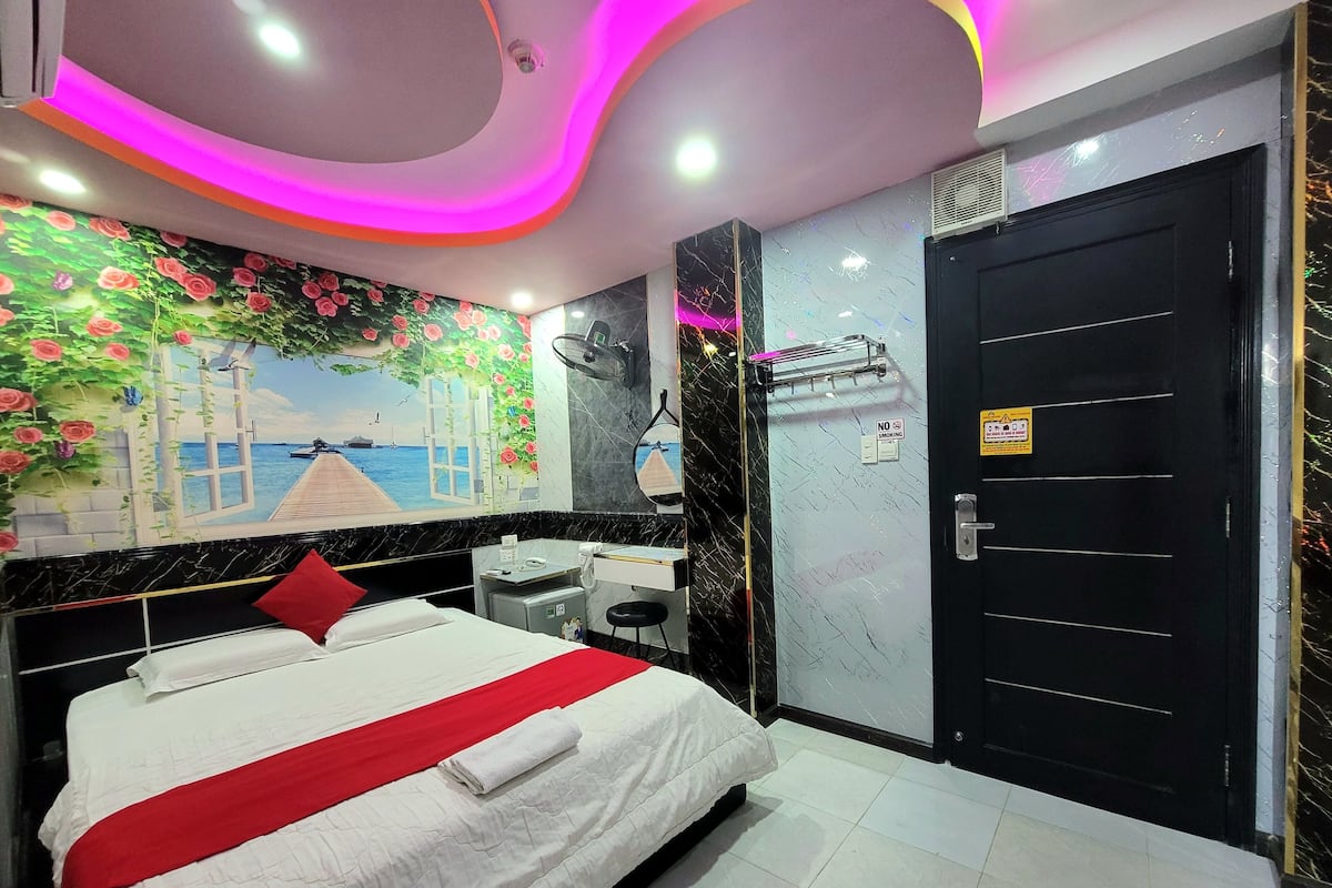 Habitación de hotel con cama, escritorio, silla, espejo, puerta y pared con un mural.