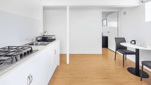 Una cocina moderna con estufa a gas, armarios blancos y piso de madera. Cuenta con un comedor con mesa y sillas.