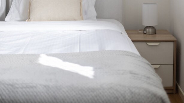 Un dormitorio minimalista con cama, mesita de noche y lámpara.