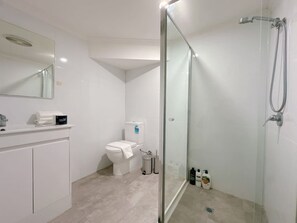 A modern bathroom with a glass-enclosed shower, a toilet, and a sink with a mirror above.