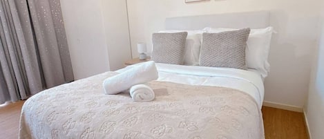 A neatly made bed with a patterned bedspread, a rolled towel, and two framed pictures on the wall.