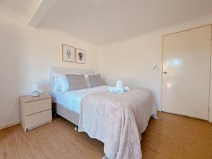 A bedroom with a bed, a bedside table, a nightstand, and a door.