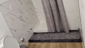 A bathroom with a marble wall, a shower curtain, a white toilet, and a wooden floor.