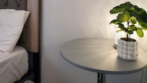 A bedroom with a bed, a round table with a potted plant, and a headboard.