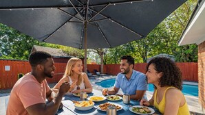 A group of people dining at an outdoor table with a pool in the background. - Amazing 4BR 2Bath Home with Pool & Game-Movie Room (Texas City)
