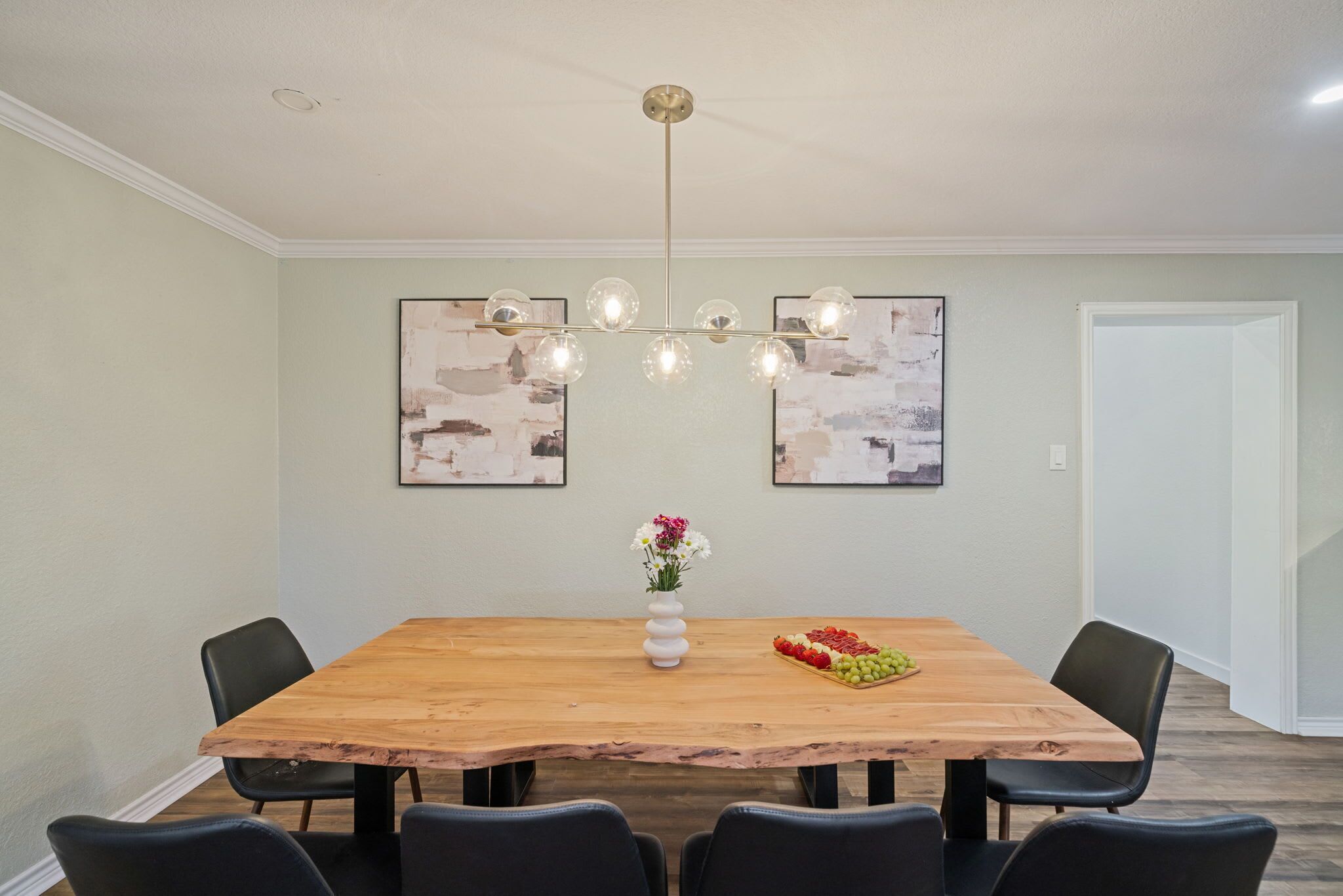 A dining area with a wooden table, black chairs, a vase with flowers, and abstract art on the wall.