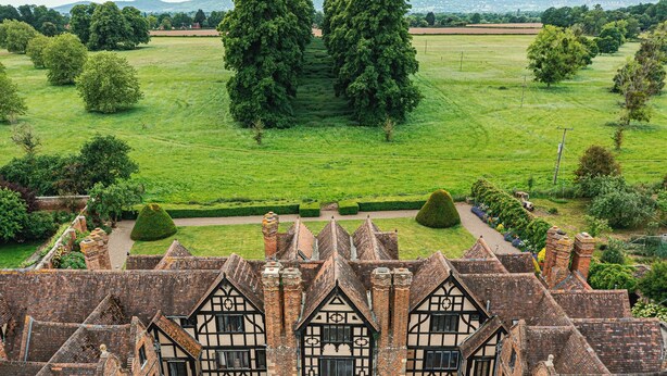A historic building with multiple gabled roofs and a large lawn with trees and a hedge. - Severn End - 15th Century Manor House (Worcester)