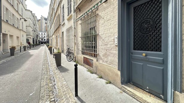 A narrow cobblestone street lined with historic buildings, a bicycle parked by the side, and a large door with a decorative grille.