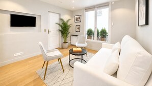 A modern living room with a white sofa, a white armchair, a small round table, and a potted plant.
