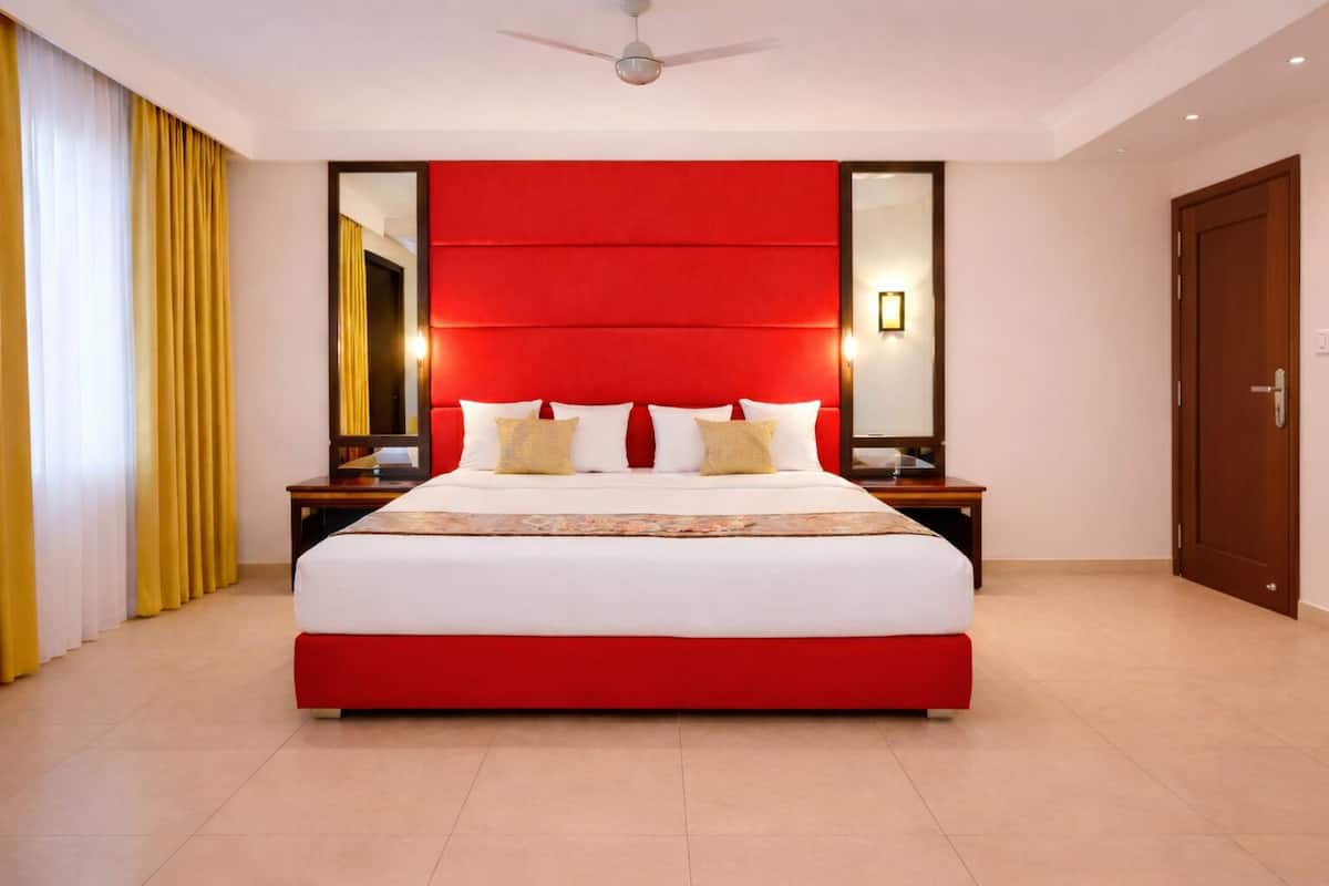 A modern hotel room with a large bed, red headboard, and a mirror above the bed.