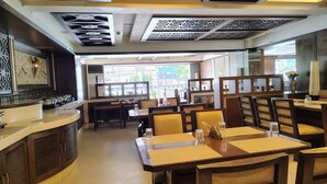 Un ristorante con tavoli e sedie di legno, un bancone con attrezzature per il servizio di ristorazione e pannelli decorativi al soffitto.