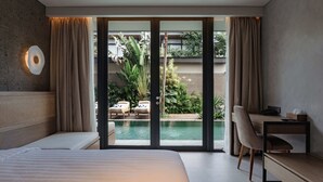 A modern hotel room with a large bed, a desk, and a view of a pool and garden.