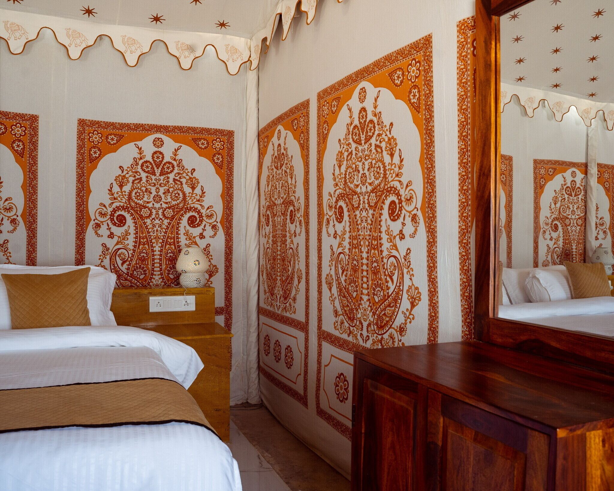 Una habitación de hotel con una cama, una mesita de noche de madera, una mesilla con lámpara y un espejo grande.