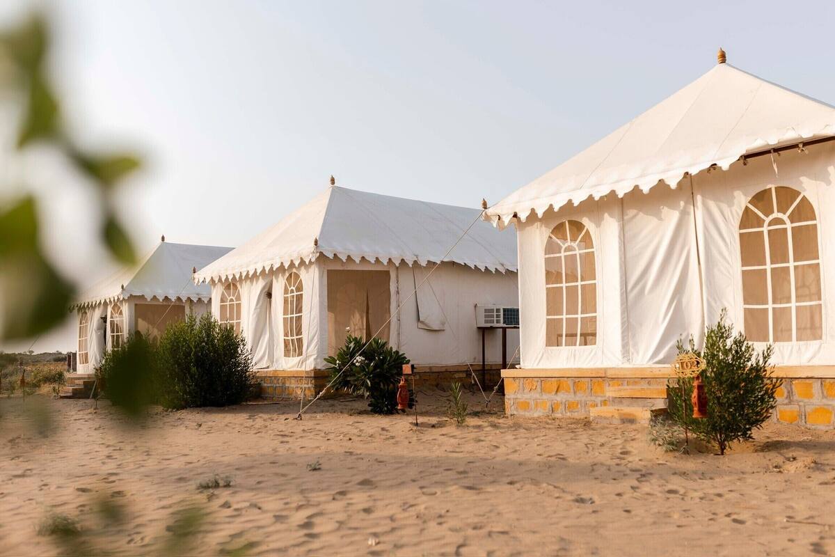 A row of white tents with large windows, set in a desert environment with sparse vegetation.