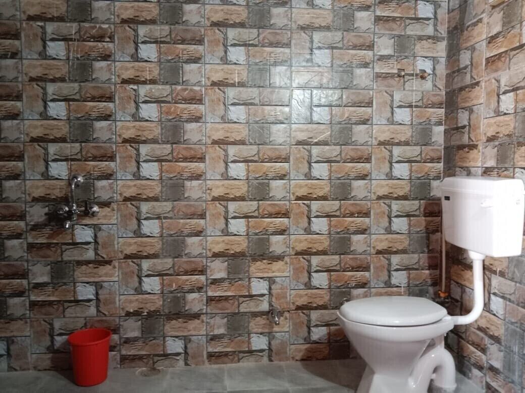 Ein Badezimmer mit einer Wand im Steinoptik, einer weißen Toilette und einem roten Eimer.