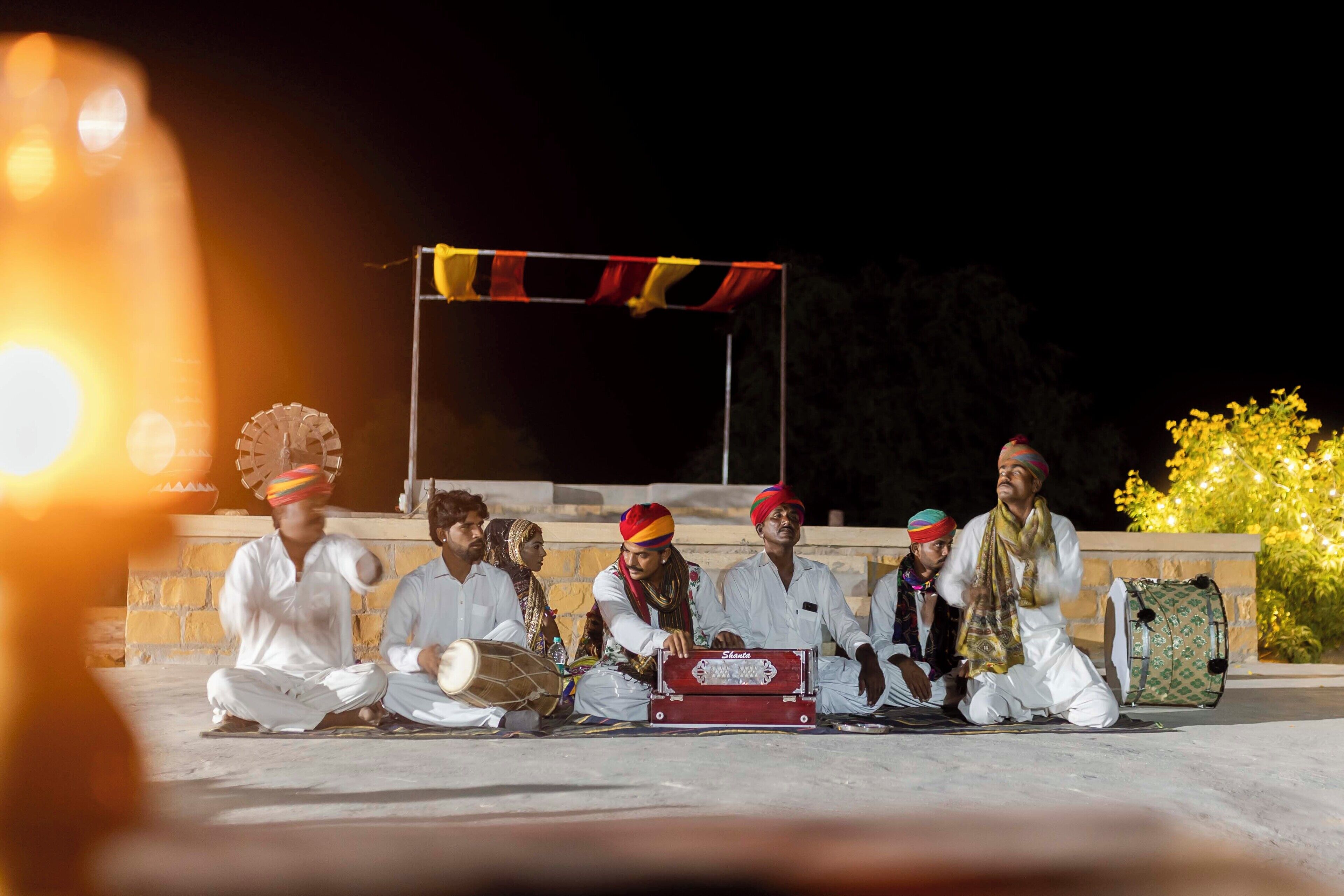 A group of people sitting on the ground outdoors at night, playing musical instruments.