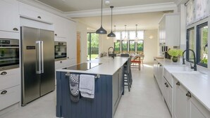 A modern kitchen with a central island, stainless steel appliances, pendant lighting, and a view to the outdoors. - Luxurious Home in Cheltenham, Private Parking (Gloucestershire)