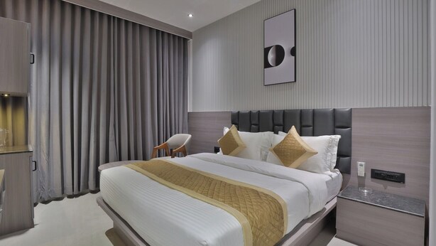 Una habitación de hotel moderna con una cama grande, cabecero, mesita de noche, una silla y una obra de arte colgada en la pared.