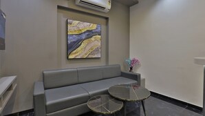 Un espace d’attente moderne avec un canapé gris, deux tables à plateaux en verre, un sol en marbre et un climatiseur fixé au mur.