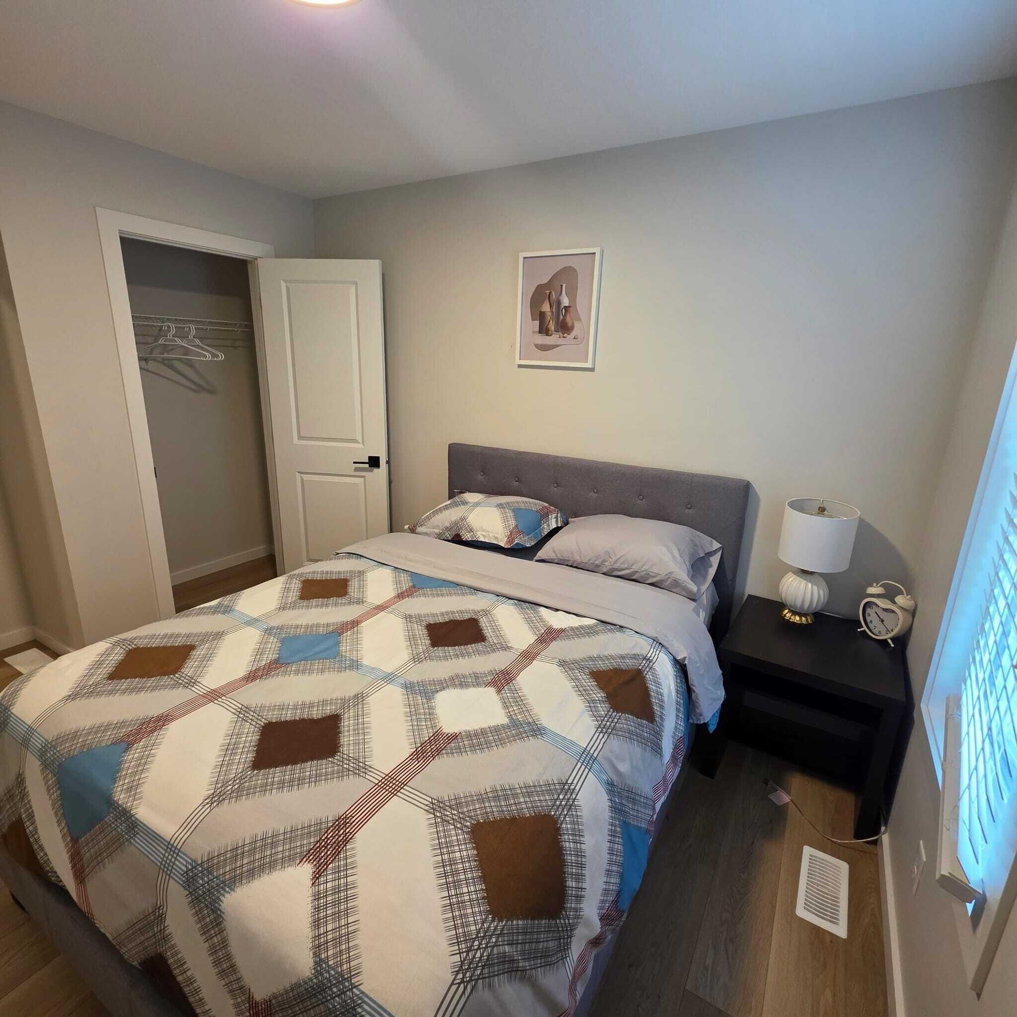 Un dormitorio con cama, mesita de noche, lámpara y un cuadro en la pared.