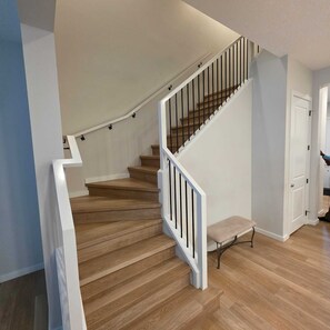 A staircase with wooden steps and white railings, leading to a landing with a bench.