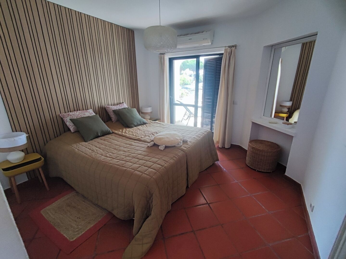 Une chambre à coucher avec un lit, une table de chevet, un miroir et une fenêtre avec des rideaux.