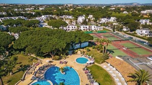 An aerial view of a resort with multiple swimming pools, tennis courts, and a large tree-covered area.