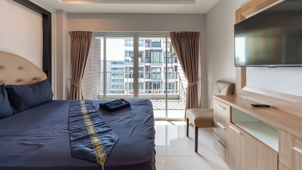 A modern hotel room with a large bed, a TV, a balcony with curtains, and a city view. - New Nordic Trend 3 (Pattaya)