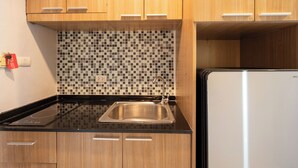 A kitchen with wooden cabinets, a black countertop, a stainless steel sink, and a white refrigerator. - New Nordic Trend 3 (Pattaya)